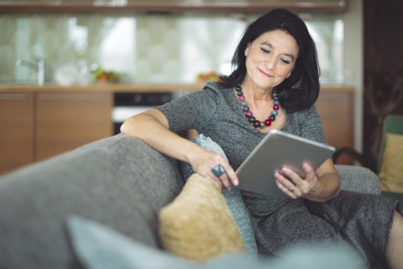 Plumbing Tips for Your Summer Rental. Woman sitting on couch on iPad.|