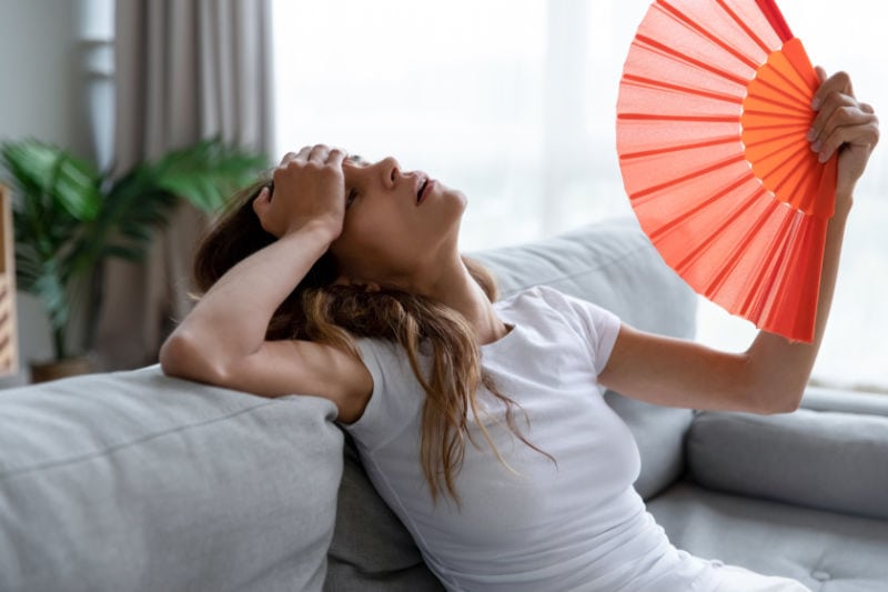 Woman overheating in her home and fanning herself with a paper fan. AC failure.