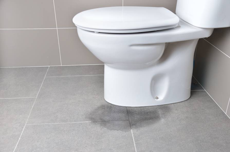 White toilet leaking water from the bottom onto the bathroom floor. Why is My Toilet Leaking From The Bottom?